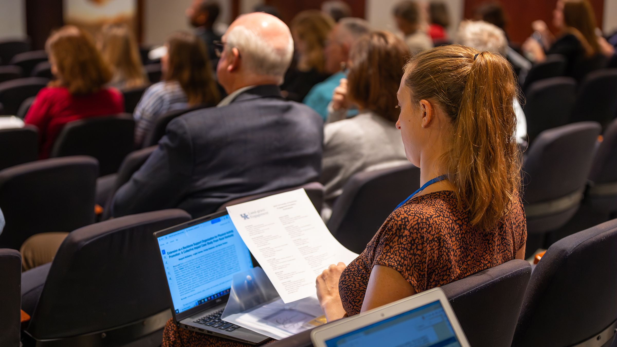 A person in the audience looks at a paper and a laptop