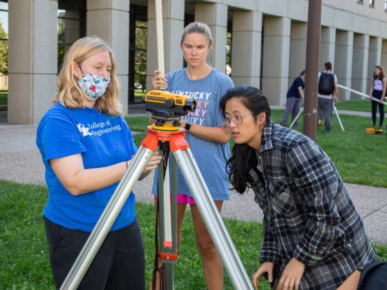 Three students examine surveying equipment